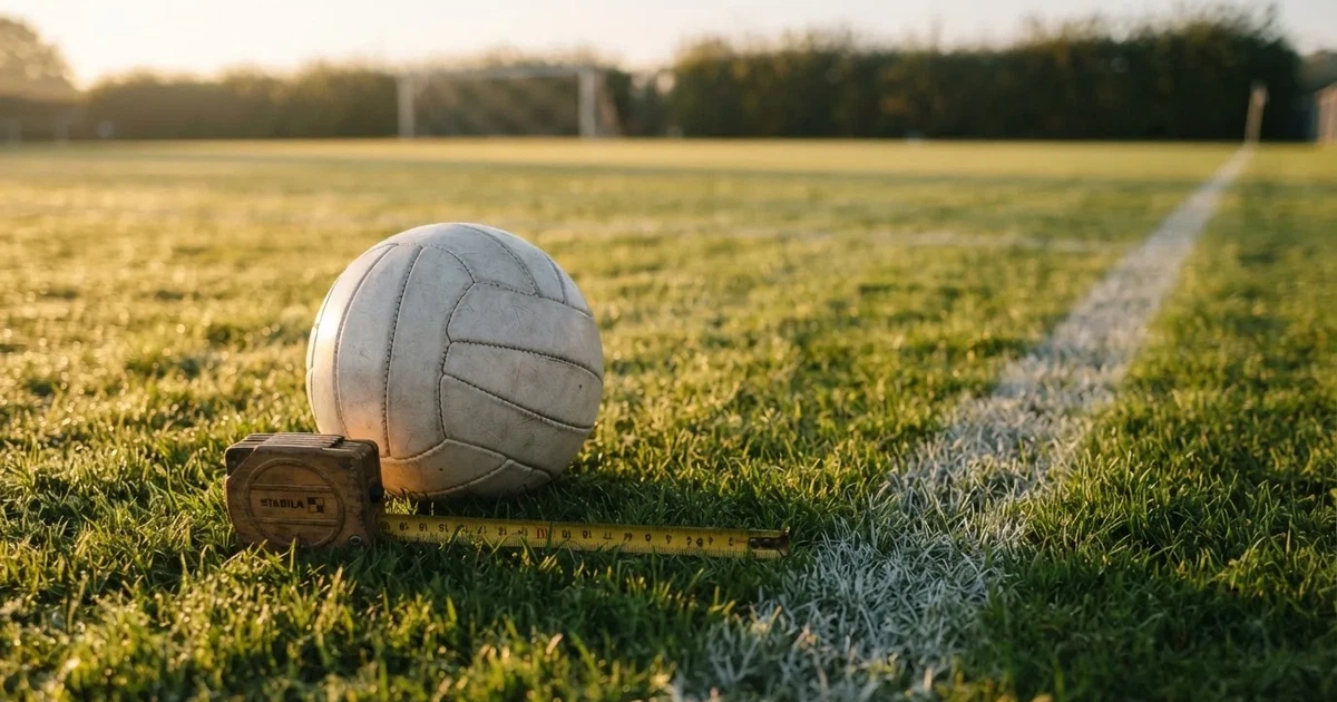 Ein Fussball und ein Massband liegen auf kurz geschnittenem Rasen neben einer Kreidelinie, Morgenlicht von der Seite.