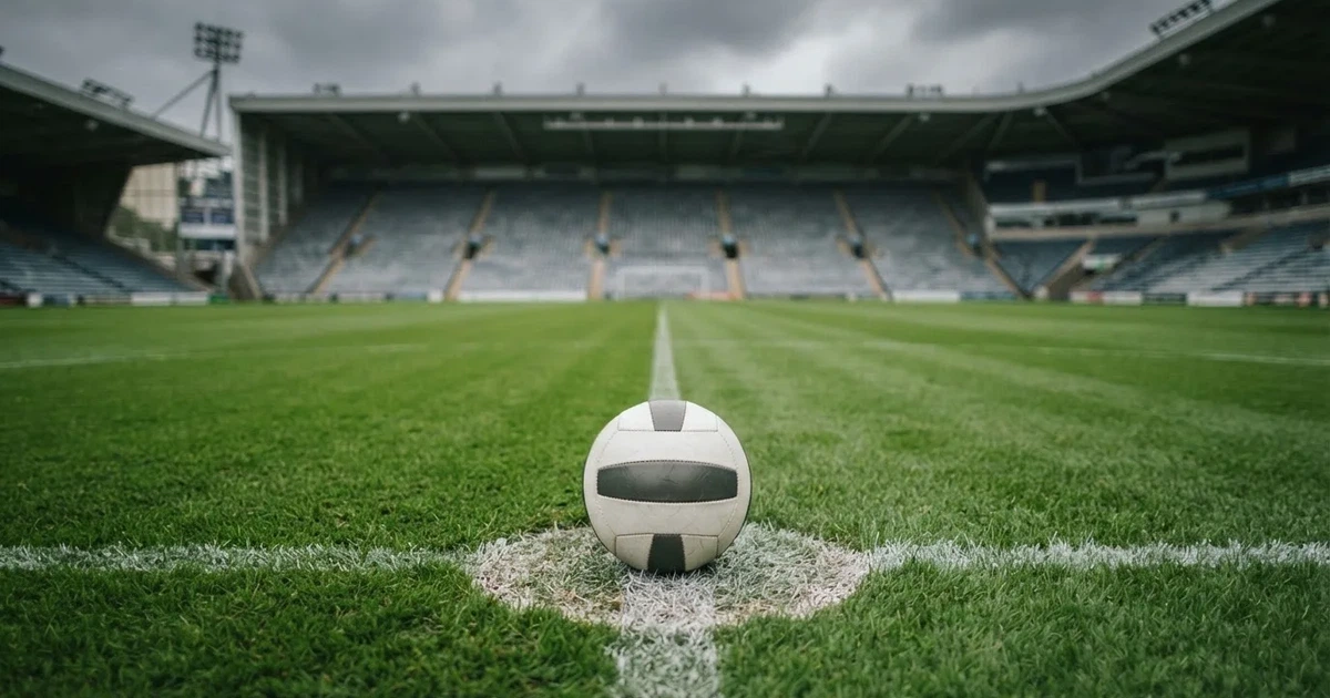 Ein Fussball liegt auf dem Anstosspunkt eines frisch gemähten Rasens, dahinter eine grosse Tribüne unter bewölktem Himmel