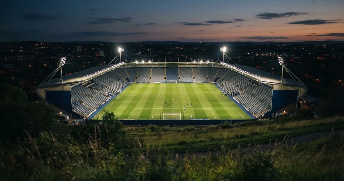 Ein Fussballstadion bei Flutlicht von einer Anhöhe aus gesehen, der Rasen leuchtet grün unter dunklem Abendhimmel