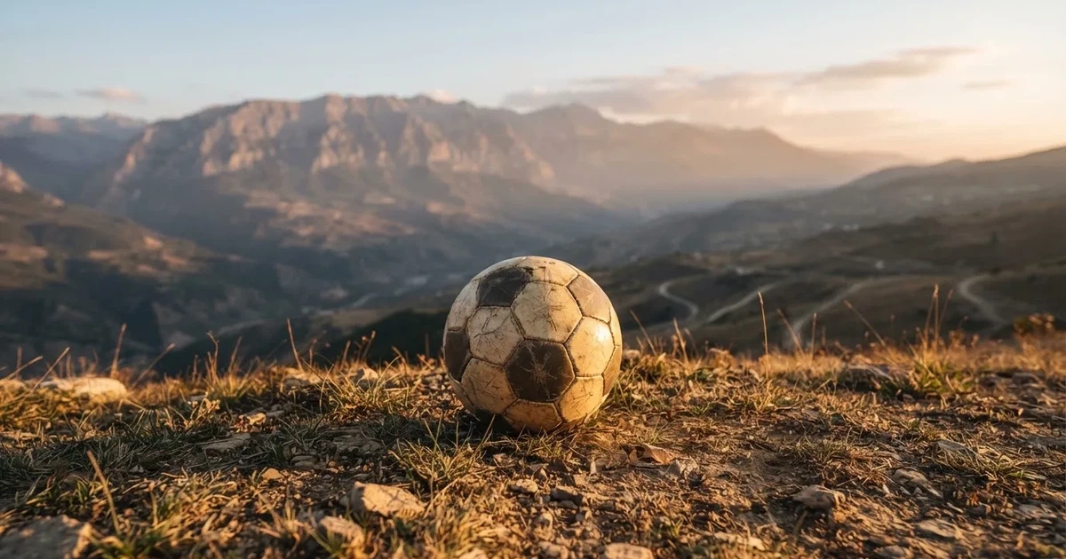 Ein Fussball auf einem staubigen Rasenstück in der Abendsonne, im Hintergrund eine hohe Bergkette